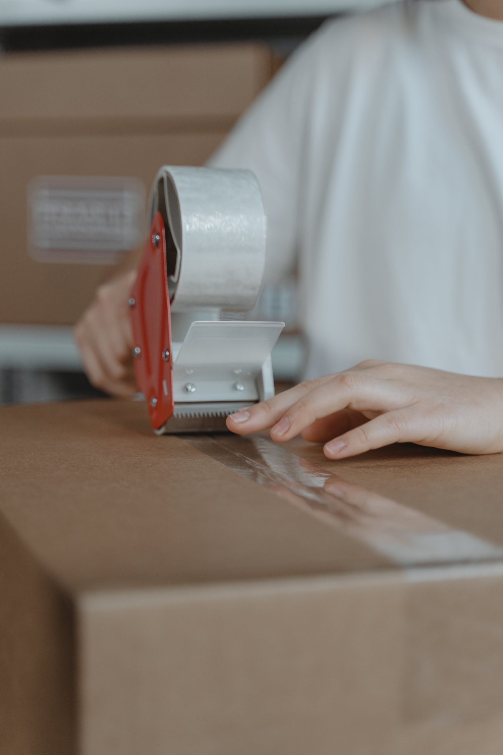 A person sealing a cardboard box with a tape dispenser in an indoor setting.